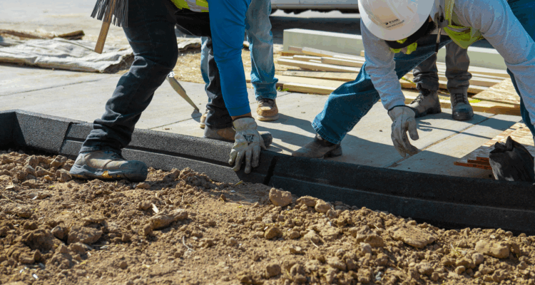 Construction workers install Hercules Eco Block between fresh dirt and sidewalk.