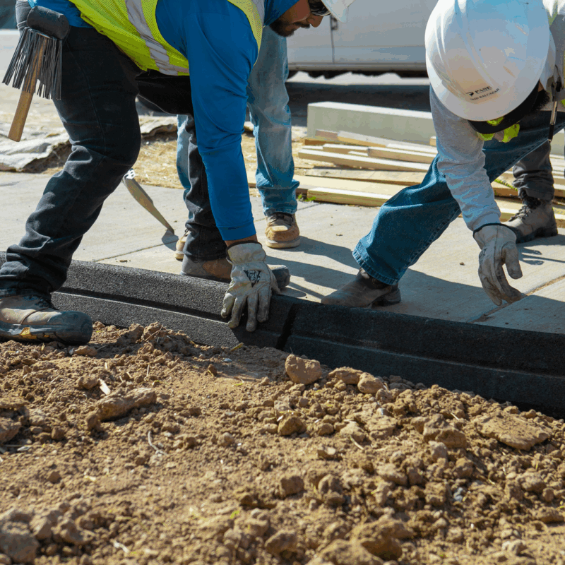 Construction workers install Hercules Eco Block between fresh dirt and sidewalk.