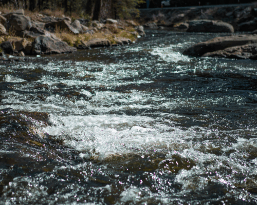 Sunlit, rocky river swiftly flows.